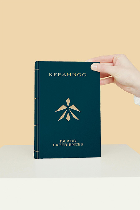 Main présentant la brochure de l'hôtel de luxe Keeahnoo intitulée Island Experiences